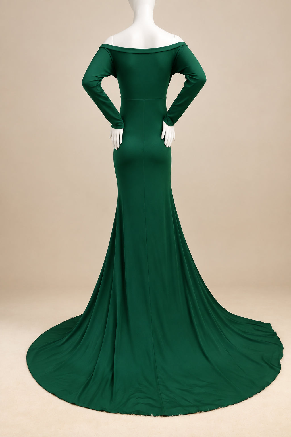 A dark green off-the-shoulder long-sleeve mermaid gown displayed on a white mannequin with a long train, set against a white wall and cream-colored rug.