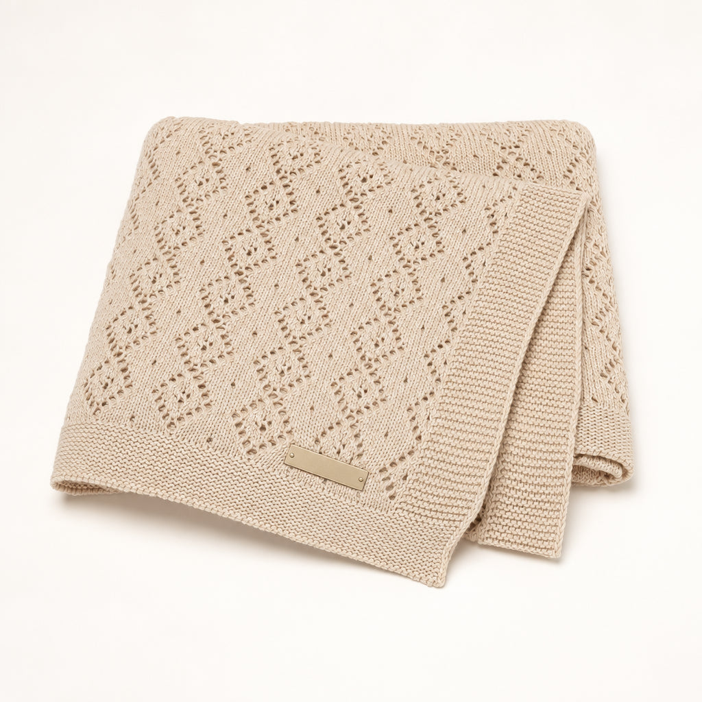 A folded beige knit blanket with a textured openwork pattern photographed on a clean white background.
