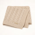 A folded beige knit blanket with a textured openwork pattern photographed on a clean white background.