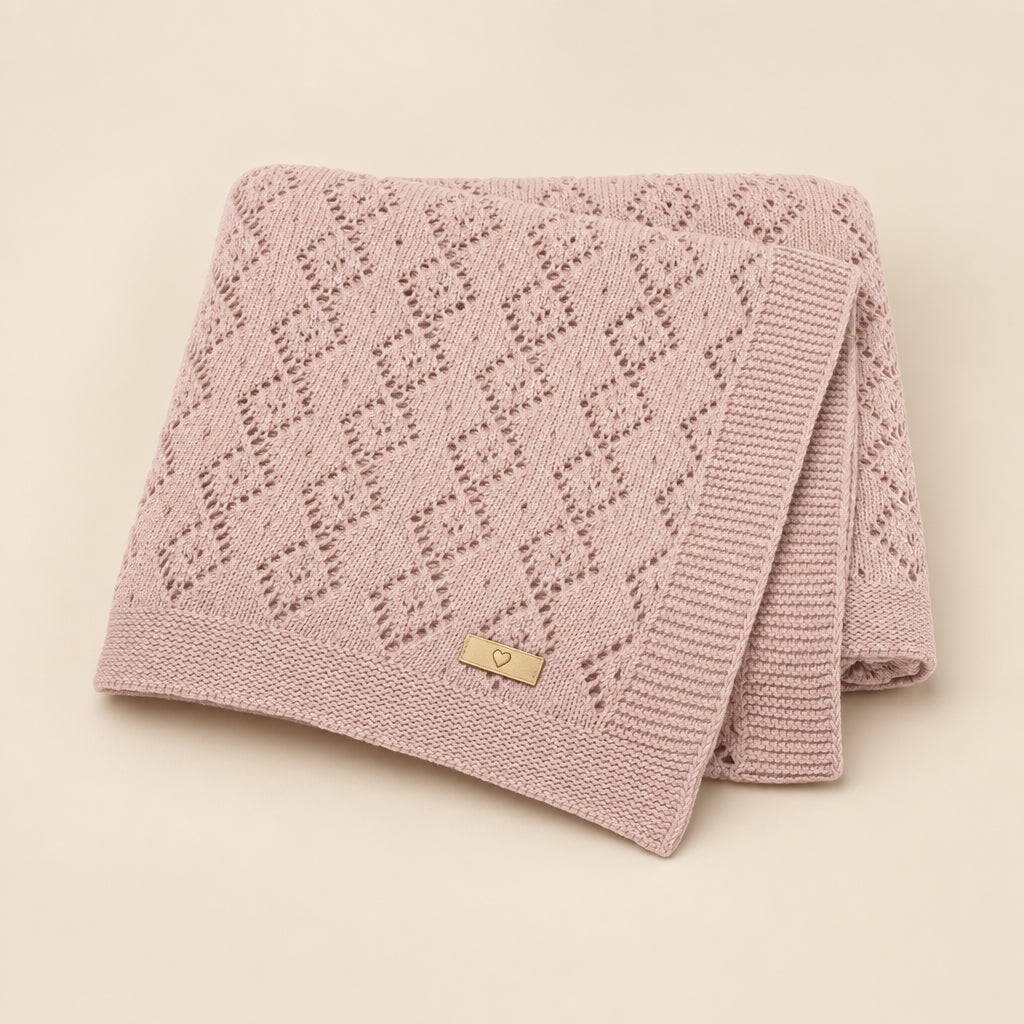 A folded dusty pink knit blanket with a textured diamond pattern and a small beige brand tag reading 'MI M. BLOOMING' on a white background.