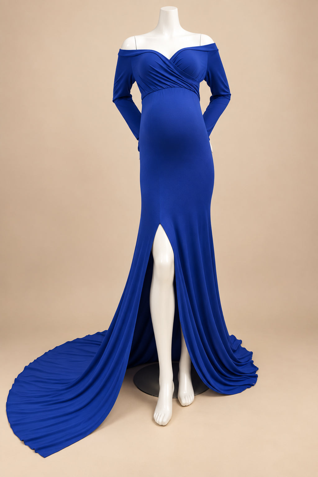 A royal blue off-the-shoulder maternity gown with long sleeves, a sweetheart neckline, and a high thigh slit, displayed on a white mannequin with a long train on a white rug.