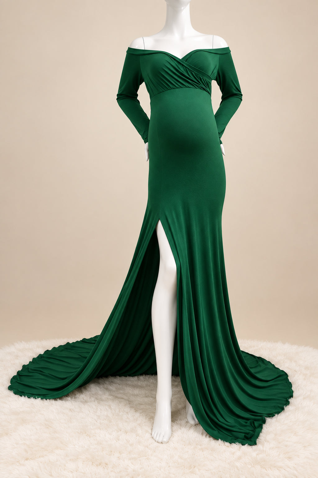 A dark green off-the-shoulder maternity gown with a sweetheart neckline, long sleeves, and a high thigh slit, displayed on a white mannequin with a long train on a white rug.