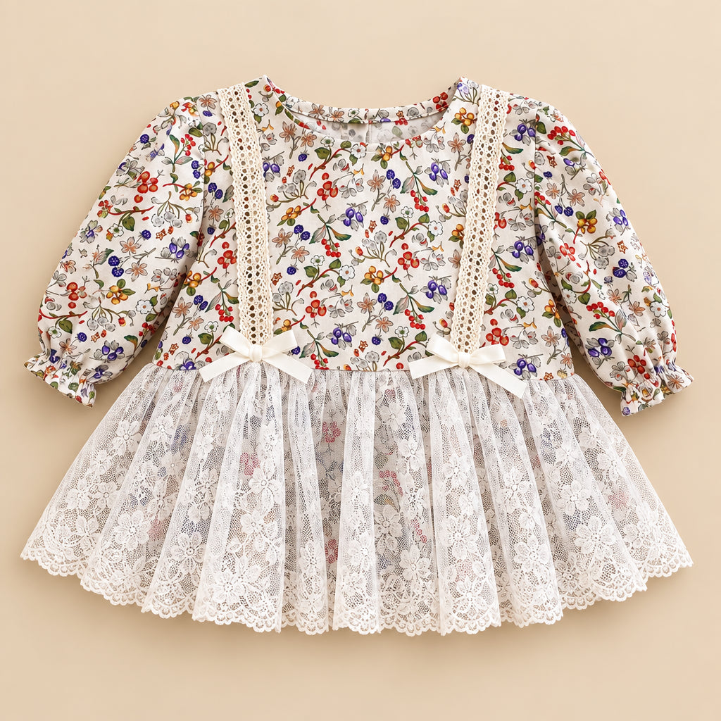 A close-up flat lay of a white dress with a dense multicolor floral print, featuring a lace-up bodice with cream ribbon bows and a layered tulle skirt. A printed magazine page is visible in the background.