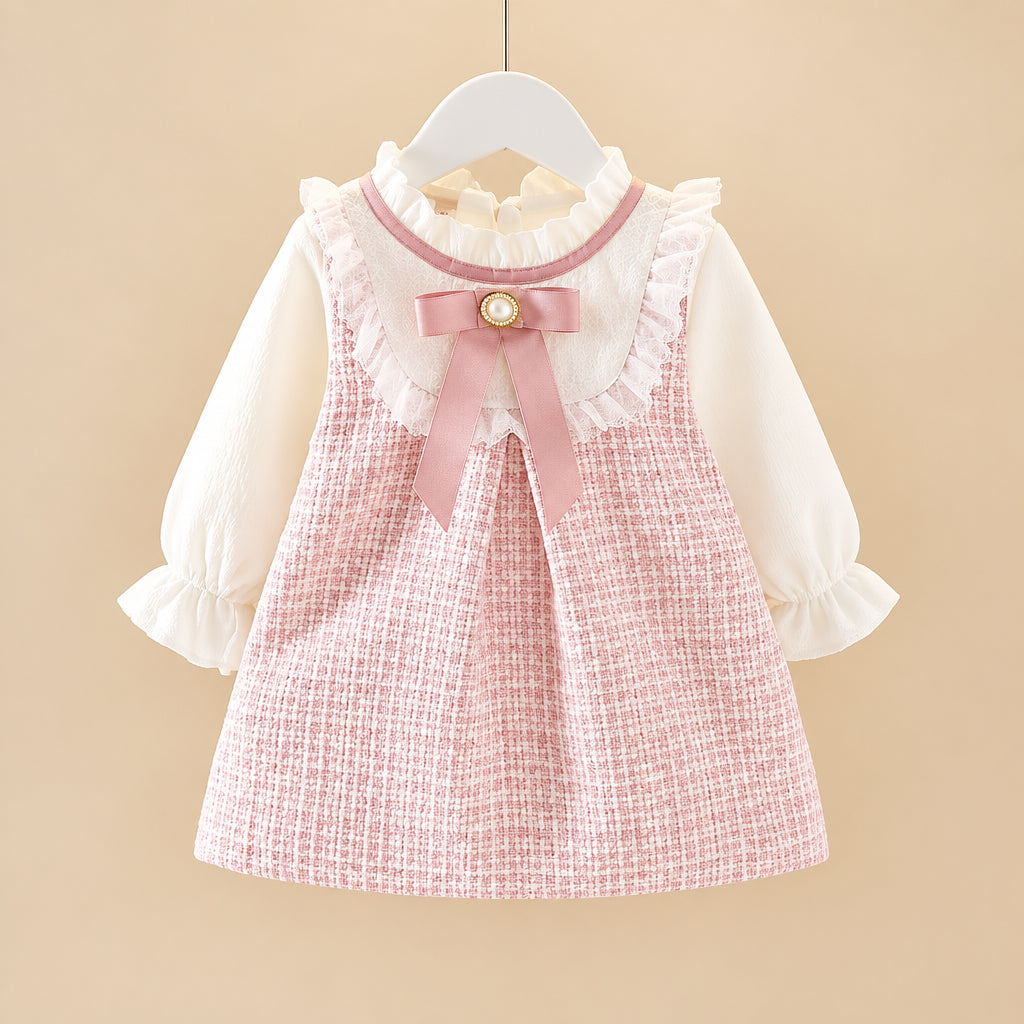 A toddler girl's two-piece outfit featuring a pink and white textured tweed pinafore vest with a pink bow and ruffled collar, layered over a white long-sleeve blouse with ruffled cuffs, hanging on a white hanger.