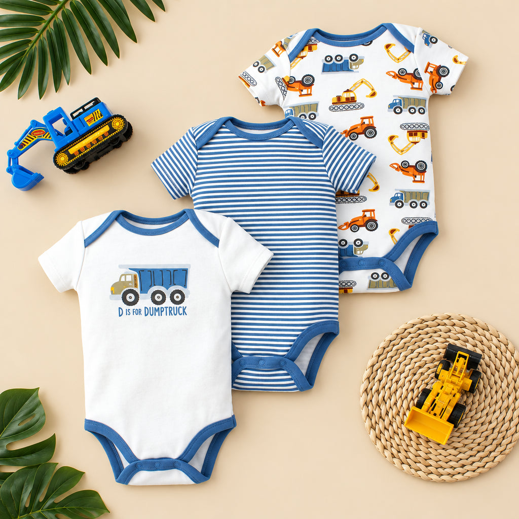 Three baby bodysuits with construction-themed designs on a light wooden surface.